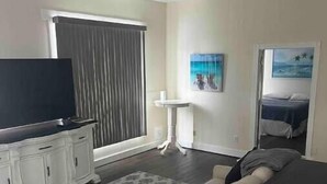 Una sala de estar con sofá, mesa de centro, televisor, una mesita auxiliar y una ventana con cortinas.
