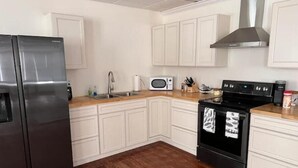 Une cuisine avec des meubles blancs, un réfrigérateur en acier inoxydable, un four à micro-ondes, une cuisinière et un plan de travail en bois.