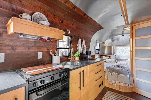 A compact kitchen with wooden cabinets, a stove, and a sink. - Airstream - (Buckeye) (Dunsmuir)
