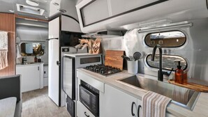 Cocina compacta con estufa, horno y lavaplatos, que cuenta con una encimera de madera y una ventana sobre el lavaplatos.