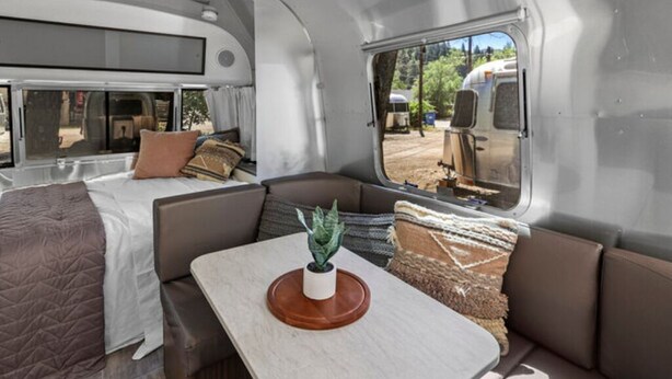 Interior compacto de una autocaravana con una cama, zona de comedor y ventana que ofrece vistas al exterior.