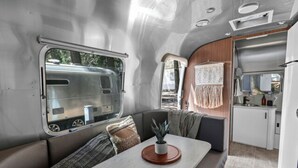 Interior compacto de una caravana con zona de comedor, kitchenette y ventana con vistas al exterior.