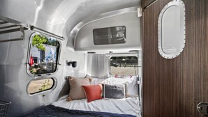 Un intérieur compact et bien éclairé d’un camping-car, avec un lit, une fenêtre et un miroir.