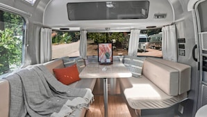 L’intérieur d’un camping-car est aménagé avec une table centrale, des sièges rembourrés et offre une vue sur l’extérieur.