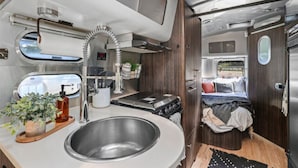 Un intérieur de camping-car compact comprenant un coin cuisine, un évier, une cuisinière et un petit espace nuit avec un lit.
