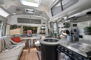 A compact kitchenette with a stove, sink, and small dining area. - Airstream - (Chestnut) (Dunsmuir)