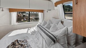 Une chambre confortable dans un camping-car, avec un lit, des oreillers et une fenêtre avec des rideaux.