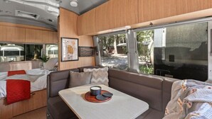 Un intérieur de camping-car compact comprenant un coin cuisine, un espace repas et un coin salon offrant une vue sur l’extérieur.