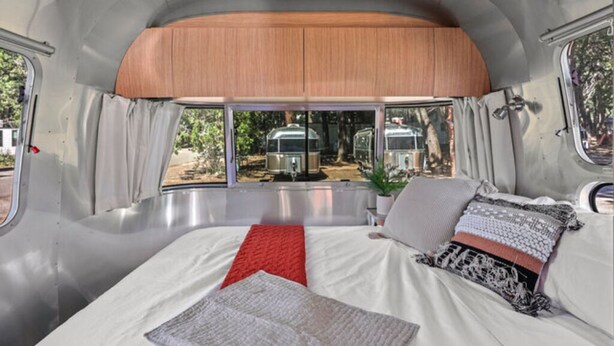 Une chambre spacieuse dans un camping-car, dotée d’un grand lit, d’une tête de lit en bois et offrant une vue sur l’extérieur.