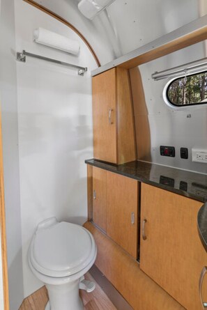 Et lille badeværelse i en autocamper med et hvidt toilet, træskabe og et lille vindue.