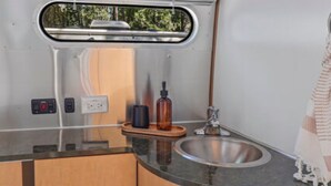 Een kleine keuken met een spoelbak, houten kastjes, een spiegel en een raam.