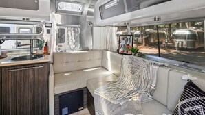 Et moderne campingvognsinteriør med et tekøkken, et siddeområde med et tæppe og et vindue med udsigt til andre campingvogne.