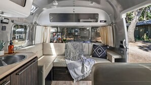 En kompakt autocamper indretning med et tekøkken, siddeområde og et vindue med udsigt til naturen.
