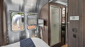 En kompakt, moderne indretning i en autocamper med en seng, et lille tekøkken og en skydedør til et badeværelse.