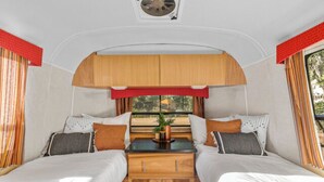 Een compact interieur van een camper, met twee bedden, een centrale tafel en een raam met uitzicht op de omgeving.