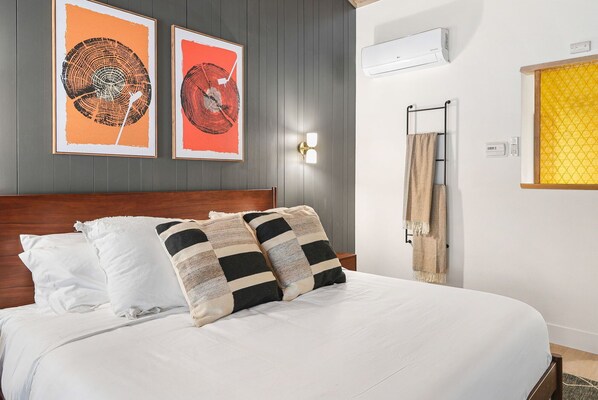 Una cama bien tendida con almohadas blancas y a rayas, un cabecero de madera y dos cuadros enmarcados en la pared.