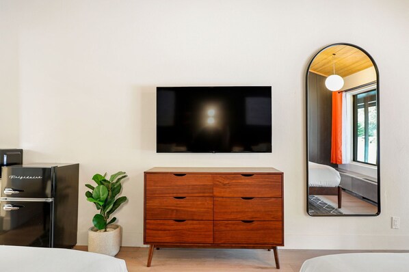 Habitación de hotel moderna con tocador de madera, televisor de pantalla plana montado en la pared y un espejo grande que refleja la vista de una ventana.