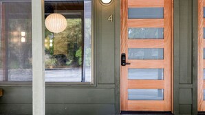 Une porte en bois avec un panneau de verre et un système de verrouillage à clavier, une fenêtre ronde avec une lampe suspendue, et un mur extérieur vert portant le numéro 4.