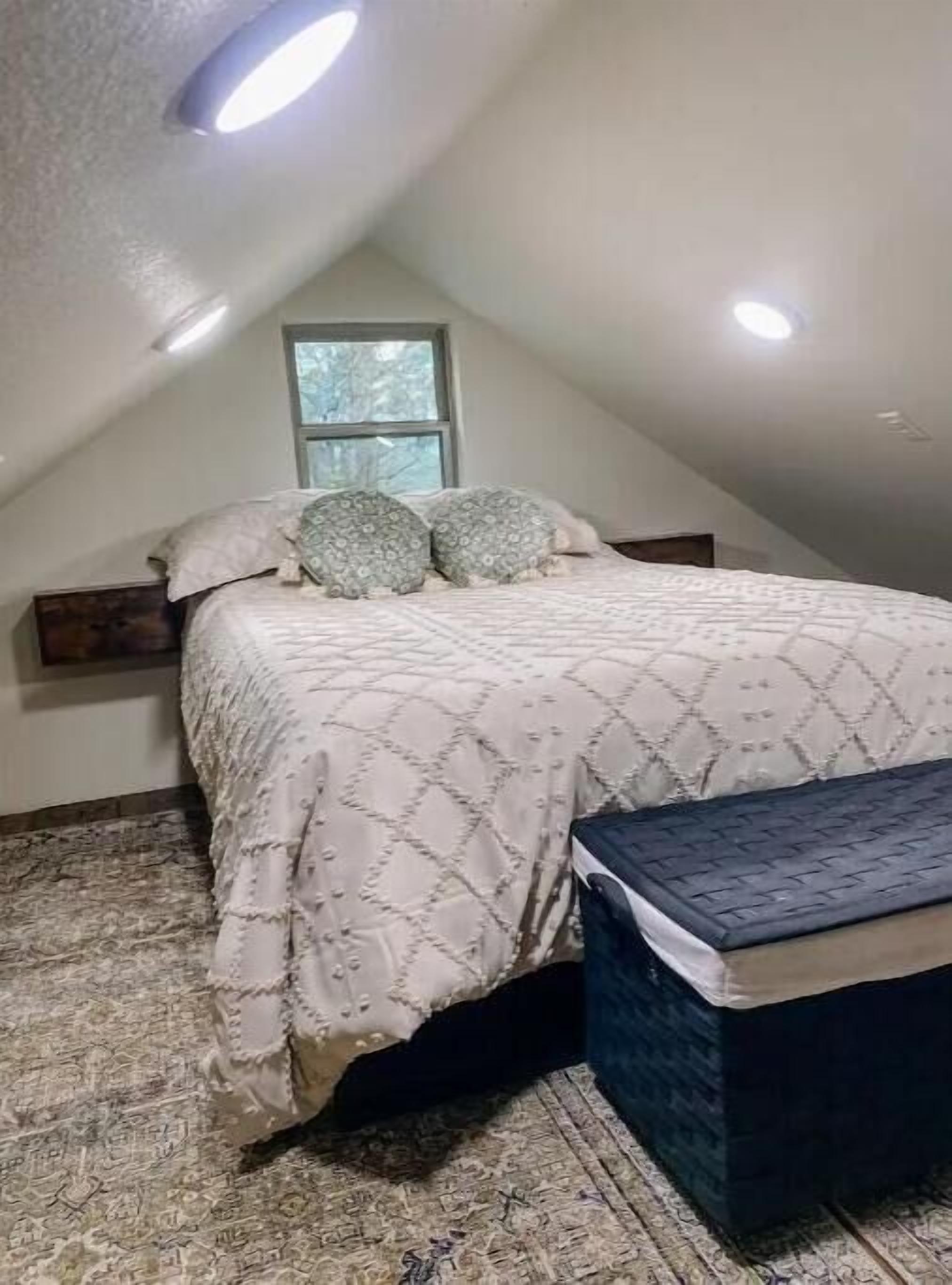 A bedroom with a bed, pillows, a bench, a window, and a ceiling light.