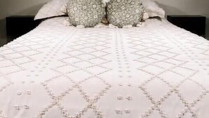A bedroom with a high ceiling, a large bed with patterned pillows, a window, and a dark headboard. - Enzo's Bungalow (Russellville)