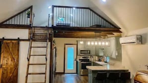 A spacious loft with a high ceiling, a mezzanine level, a kitchen with modern appliances, and a bar area. - Enzo's Bungalow (Russellville)