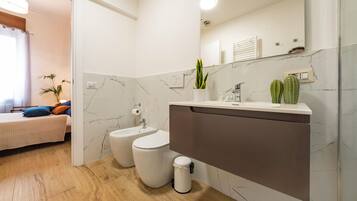 Une salle de bain moderne avec un pare-baignoire en marbre, un lavabo blanc et un bidet.