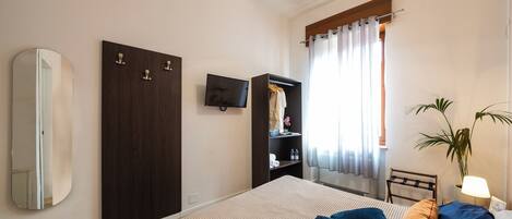 Une chambre à coucher avec un lit, une télévision, une armoire et une fenêtre avec des rideaux.