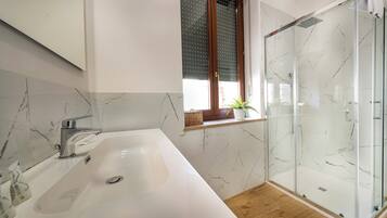 A bathroom with a white sink, a glass shower enclosure, and a window with blinds.