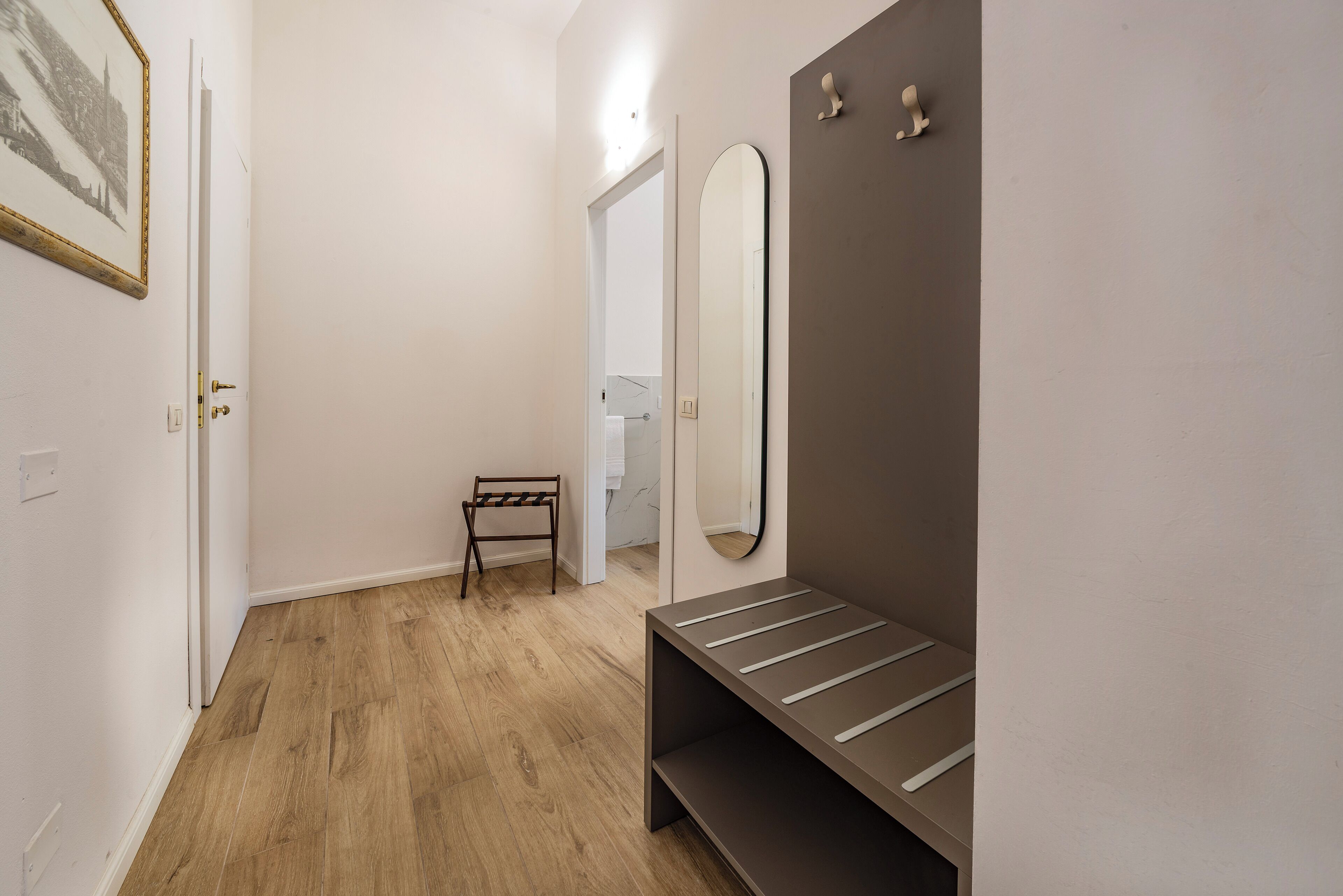 A hallway with a wooden floor, a bench, a coat rack, and a mirror.