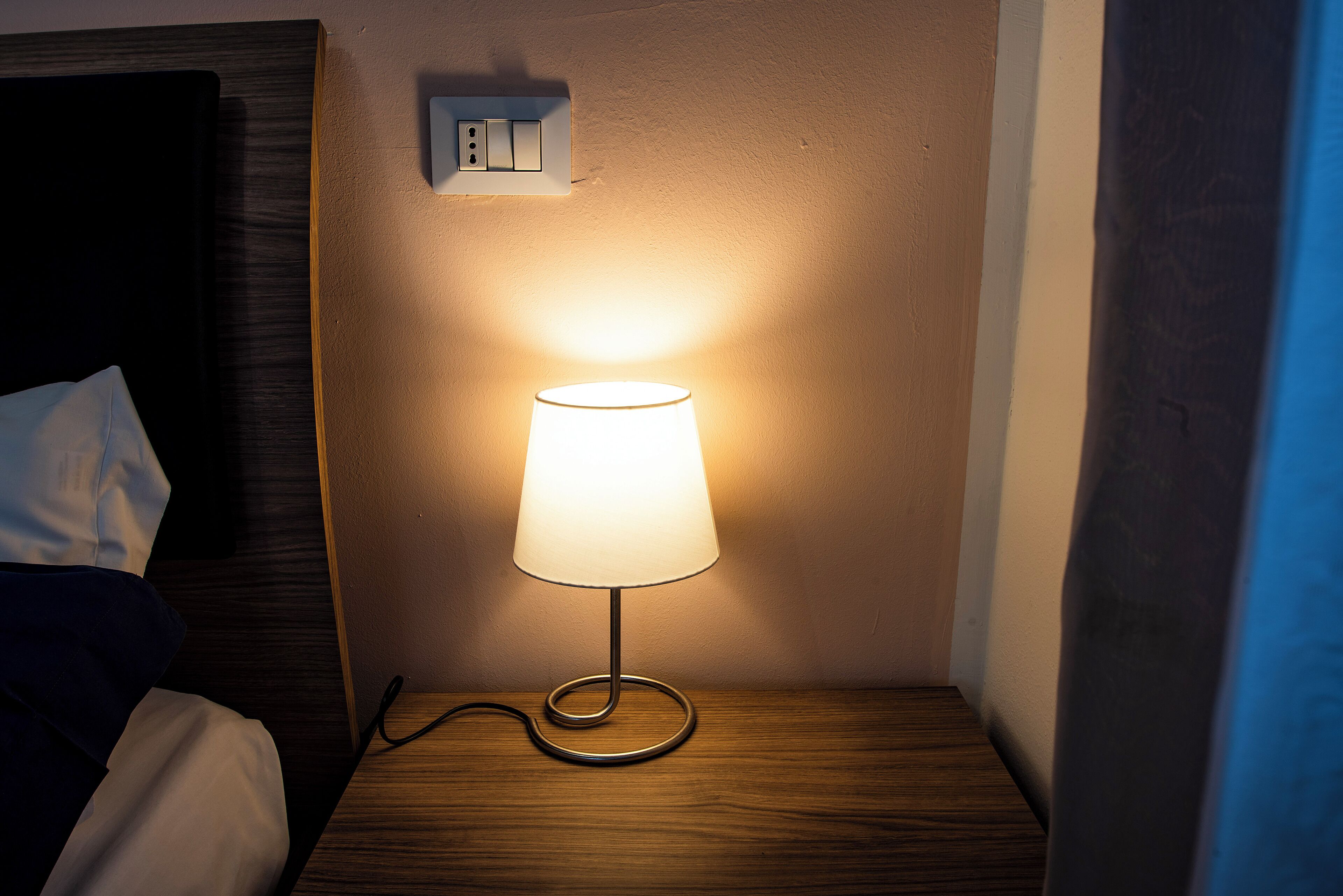 A bedside table with a lamp, a power outlet, and a wooden headboard.