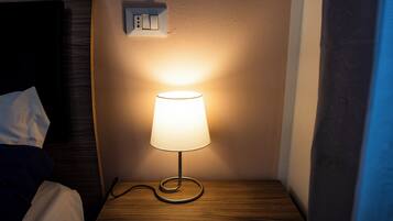 A bedside table with a lamp, a power outlet, and a wooden headboard.