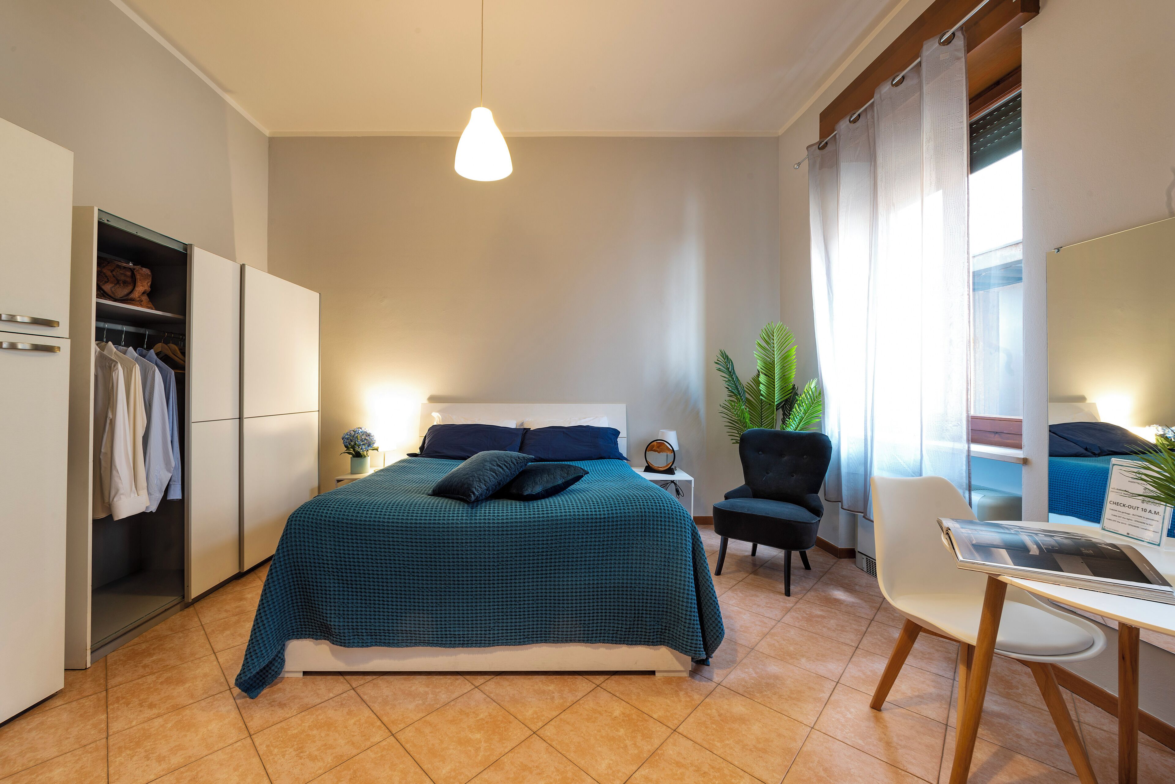 Ein Schlafzimmer mit einem Bett, Nachttischen, einem Schreibtisch, einem Stuhl, einem Kleiderschrank und einer Hängelampe.