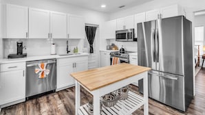 A modern kitchen with white cabinets, stainless steel appliances, and a wooden table.