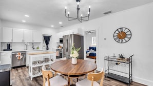 A modern kitchen with white cabinets, a wooden dining table, and a black metal cart.