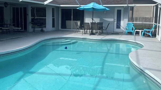 A covered outdoor swimming pool with a blue umbrella, surrounded by patio furniture and chairs. - Rare & Amazing 3 bdrm 2 bath apt with pool gives you a home away from home feel. (Lutz)