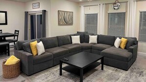 Olohuoneessa on kulmasohva, sohvapöytä, ruokapöytä tuoleineen ja kattotuuletin.