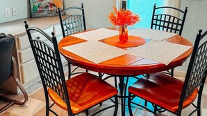 A dining area with a round table, four chairs, and a vase with orange flowers.