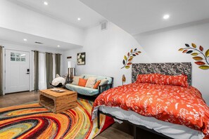 Ein modernes Schlafzimmer mit einem großen Bett, einer Couch, einem Holztischchen und einem farbenfrohen Teppich.