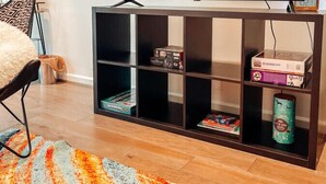 A living room with a flat-screen TV on a wooden stand, a patterned rug, and a bookshelf with various items.