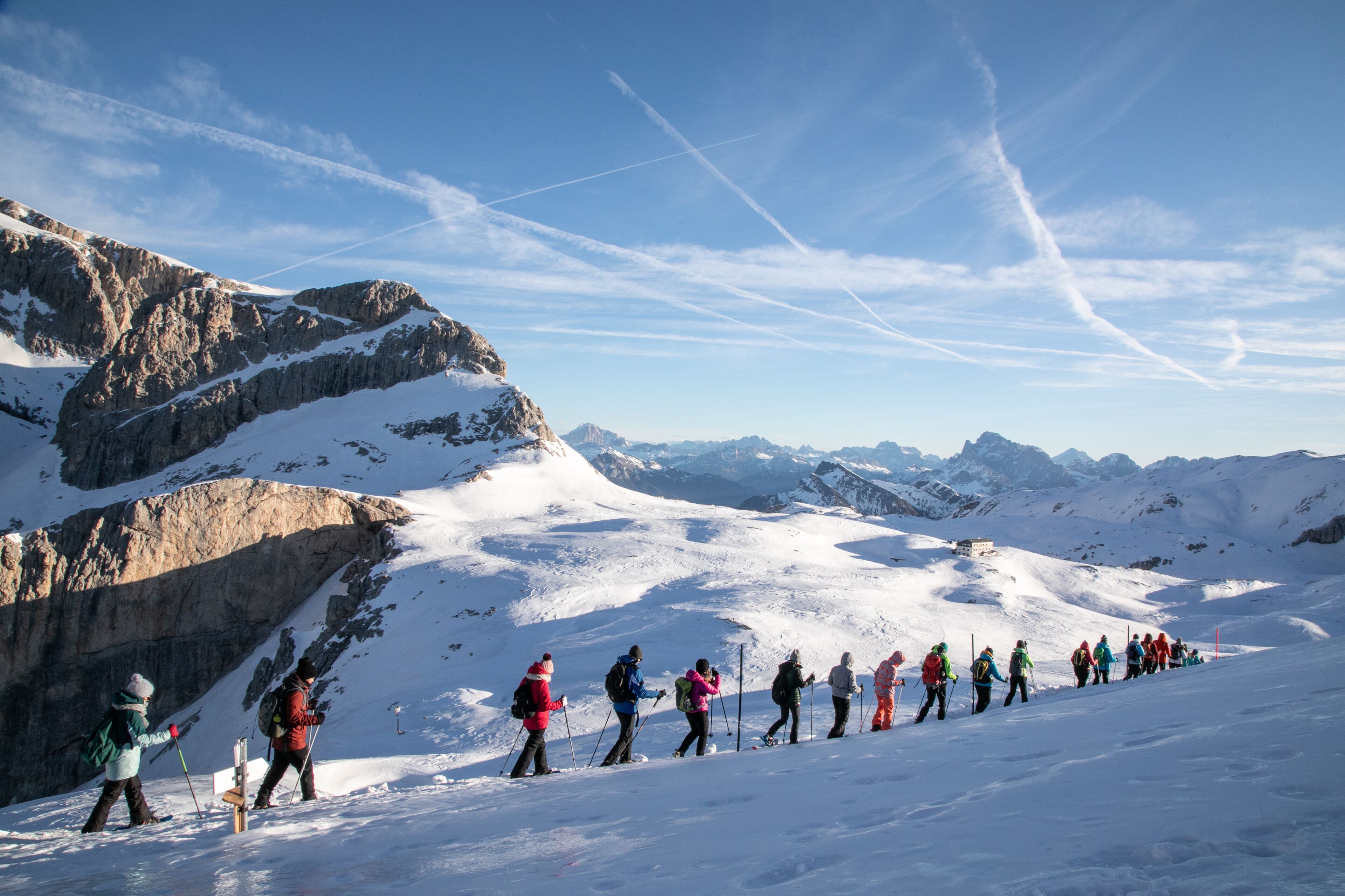 A group of skiers on a snowy mountain slope with rocky terrain and distant peaks.