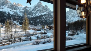 Un paysage de montagne enneigé vu à travers une fenêtre, agrémenté d’une décoration en forme d’étoile et d’un luminaire suspendu.