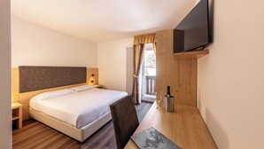 Une chambre d’hôtel avec un lit, un bureau avec un ordinateur portable, une télévision et une fenêtre avec des rideaux.