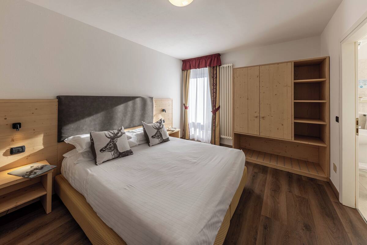 A bedroom with a large bed, wooden headboard, bedside tables, a wardrobe, and a window with curtains.