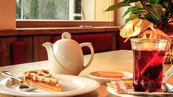 A table with a teapot, a slice of pie, a glass of tea, and a plate with an orange slice.