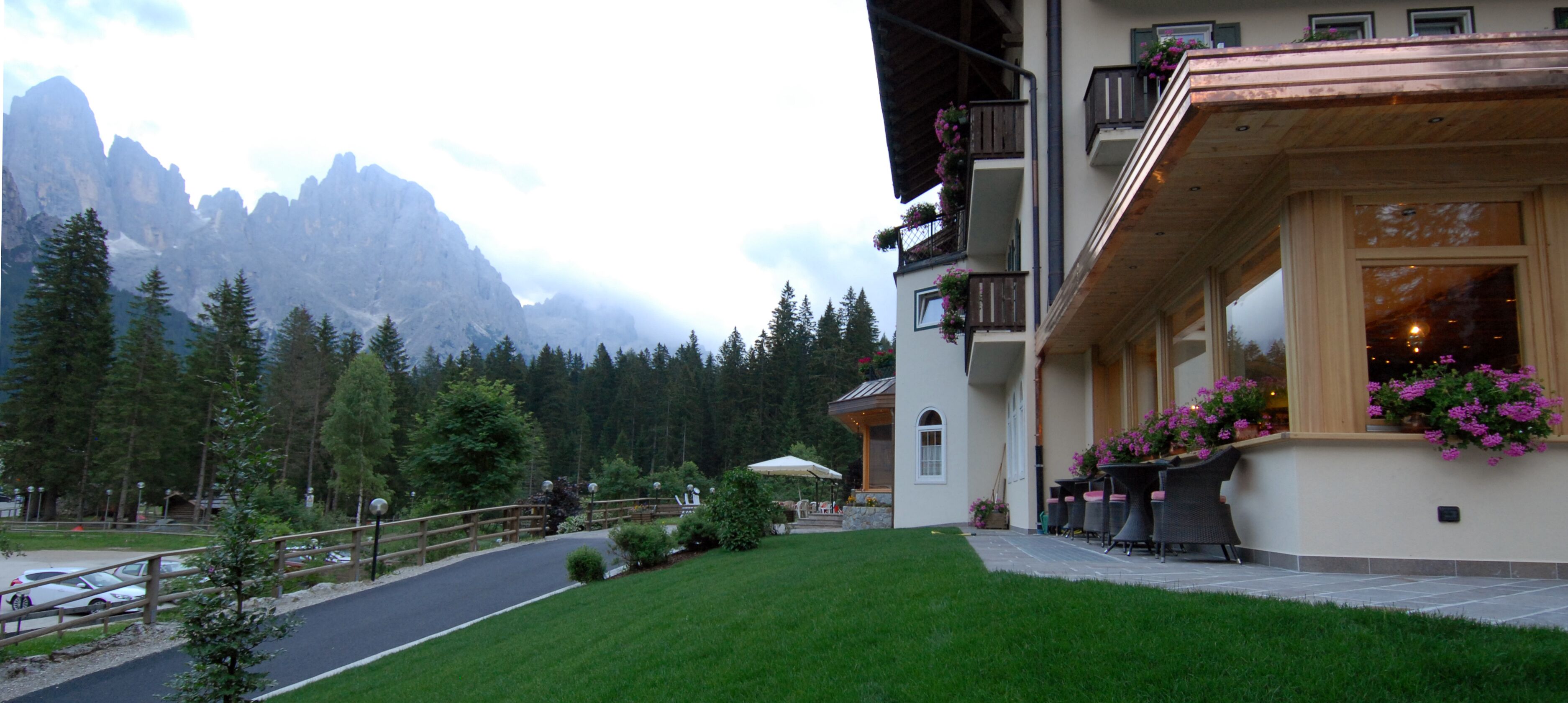Un hotel con vistas a la montaña, camino de entrada pavimentado y mobiliario exterior con flores.
