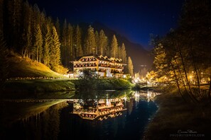 A large, multi-story hotel with a reflection in the water, surrounded by trees and a mountain in the background. - Hotel Plank (Primiero San Martino di Castrozza)