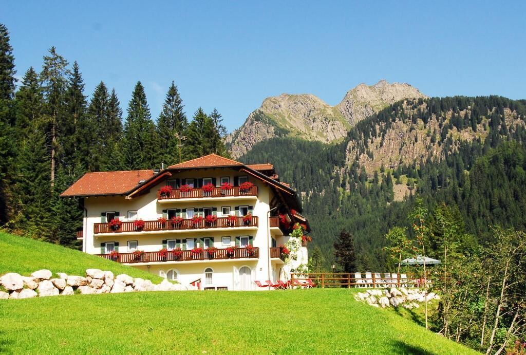 A multi-story hotel with balconies, set against a mountainous backdrop.