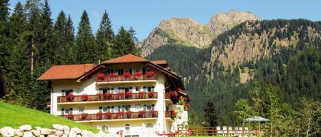 A multi-story hotel with balconies, set against a mountainous backdrop.