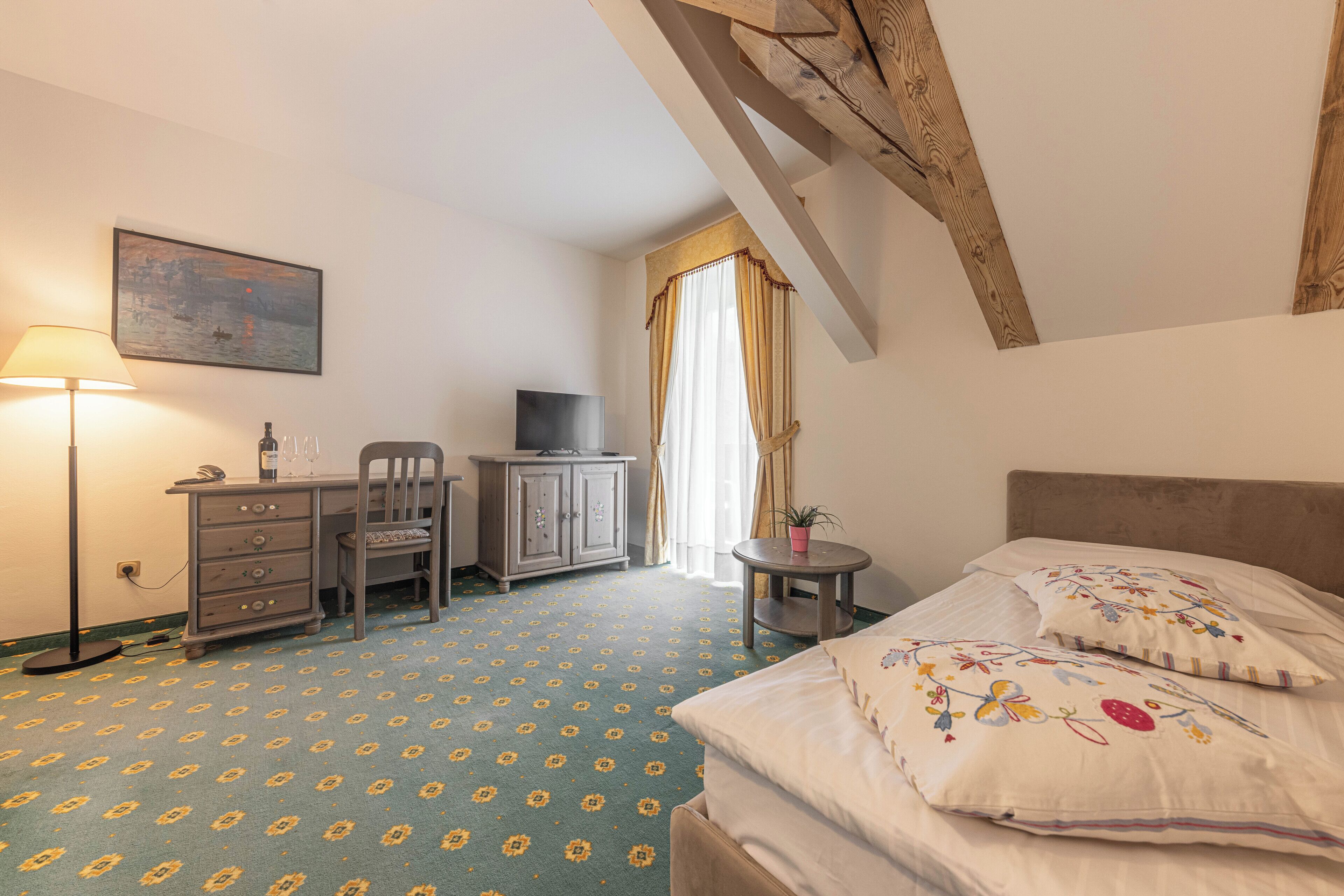 Une chambre d’hôtel avec un lit, un bureau, une chaise, une télévision et une fenêtre avec des rideaux.