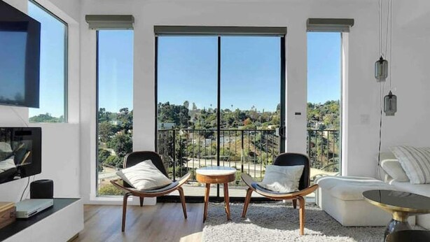 Una sala de estar moderna con balcón, ventanas grandes y televisor de pantalla plana.